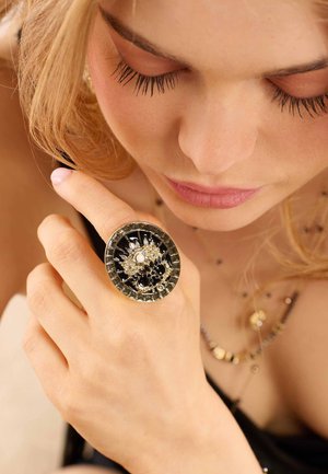 Round ring featuring a black center embellished with a floral design made of gold-tone and pearl accents; textured band.