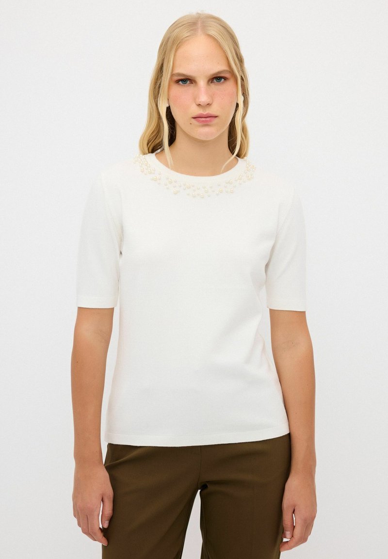 Vit kortärmad topp med rund halsringning och dekorativa pärlliknande detaljer runt kragen. Slät, stretchig tyg.