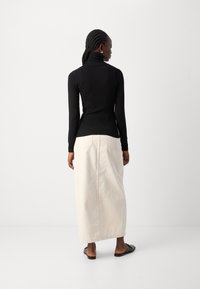 Zwarte geribbelde lange mouwen coltrui gecombineerd met een luchtige crèmekleurige midirok met een split aan de achterkant en casual platte sandalen.