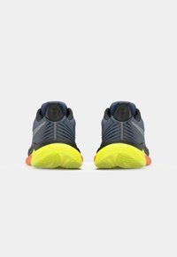 Zapatillas deportivas con un upper de malla texturizada en azul marino, detalles en negro y un diseño de suela en amarillo brillante, naranja y gris. Incluyen detalles reflectantes.