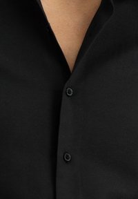 Camicia nera con bottoni, caratterizzata da un colletto classico, tessuto testurizzato, due bottoni neri e un design pulito e sartoriale.