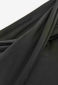 Zwart doek met een gladde, licht gestructureerde oppervlakte, voorzien van overlappende plooien die diepte en dimensie creëren.