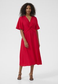 Red midi dress with a twist knot bodice, short flutter sleeves, and a flowing texture. Paired with black strappy high-heeled sandals.