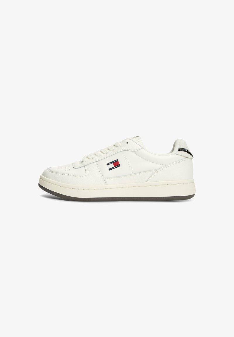 Baskets blanches basses avec un design à lacets, logo Tommy Jeans noir et rouge sur le côté, et languette de talon rayée noire.