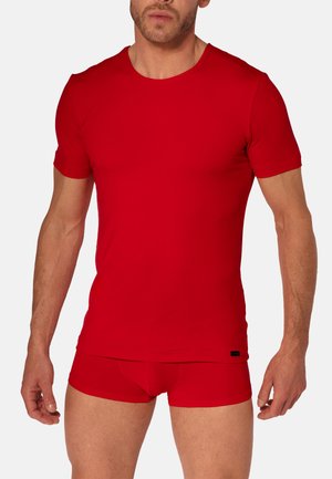 Man wearing a fitted red short-sleeve T-shirt and matching red boxer briefs, standing against a plain light background.