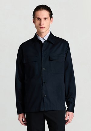 Marineblaue Hemdjacke aus leichtem Stoff mit zwei Brusttaschen, spitzem Kragen und langen Ärmeln. Einfaches, funktionales Design.