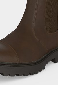 Botte en cuir marron avec panneau latéral élastique, coutures durables et semelle extérieure noire épaisse à crampons profonds pour une bonne adhérence.
