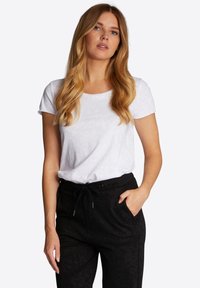 Wit T-shirt met korte mouwen van zachte stof, gecombineerd met zwarte broek met trekkoord, voorzien van een subtiel patroon en zijzakken.