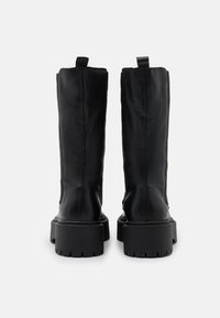 Svarta läderstövlar som går upp till knäna med en texturerad yta, har en chunky sula och dragflikar baktill. Robust och stilren design.