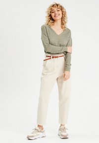 Maglione lavorato a maglia verde chiaro con scollo a V, abbinato a pantaloni beige a vita alta e sneakers color crema con dettagli marroni.