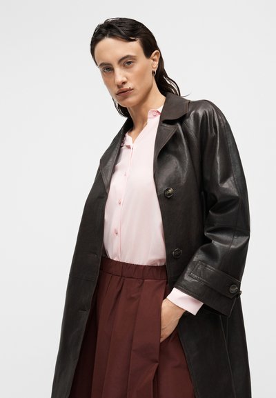 Καφέ δερμάτινο παλτό τύπου trench, ροζ μπλούζα με κουμπιά και μωβ φούστα με πιέτες. Υφασμα με υφή και έντονα κουμπιά.