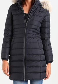Puffer coat in black with horizontal quilted pattern, hood with faux fur trim, front zipper, and knit cuff accents.
