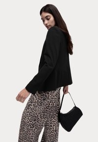 Černý blazer se strukturovanými rameny a hladkým materiálem, spárovaný s širokými kalhotami s leopardím potiskem a texturovanou černou kabelkou.