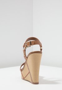 Sandale en wedge marron avec une sangle de cheville beige texturée, présentant un design géométrique et des coutures rouges contrastantes sur le wedge.