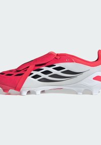 Κόκκινο και λευκό ποδοσφαιρικό παπούτσι με επάνω μέρος από δίχτυ, μαύρες λεπτομέρειες, σταθερό λουρί και διαμορφωμένες οστίδες για πρόσφυση.