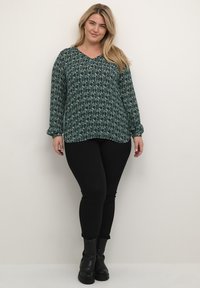 Grøn langærmet bluse med blomstermønster, V-hals-design og fitted ærmer. Sammen med sorte skinny jeans og ankelstøvler.