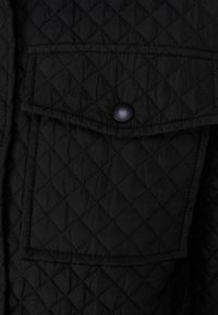 Černá prošívaná bunda s diamantovým vzorem, náprsní kapsou s klopou a černým patentním knoflíkem. Hladká textura, lehká látka.