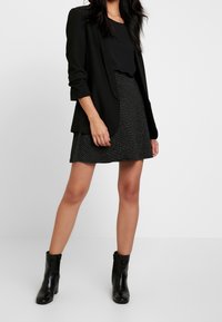 Černý blazer přes černý top, doplněný o třpytivou černou sukni. Obsahuje černé kožené boty do kotníků. Jednoduchý, strukturovaný design.