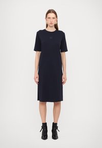 Tummansininen, polvipituinen mekko, jossa on lyhyet hihat, pyöreä pääntie ja hienovarainen logodiili rinnassa. Sileä kankaan rakenne.