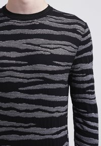 Czarny sweter z falistym szarym wzorem; wykonany z dzianiny, z okrągłym dekoltem i długimi rękawami. Teksturowana powierzchnia dodaje wizualnego zainteresowania.