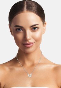 Sølv halskæde med en sommerfugle vedhæng, der har detaljerede udskårne designs. Modellen har glat hud og bærer naturlig makeup.