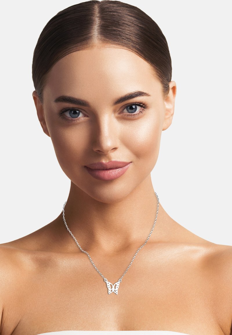 Sølv halskæde med en sommerfugle vedhæng, der har detaljerede udskårne designs. Modellen har glat hud og bærer naturlig makeup.