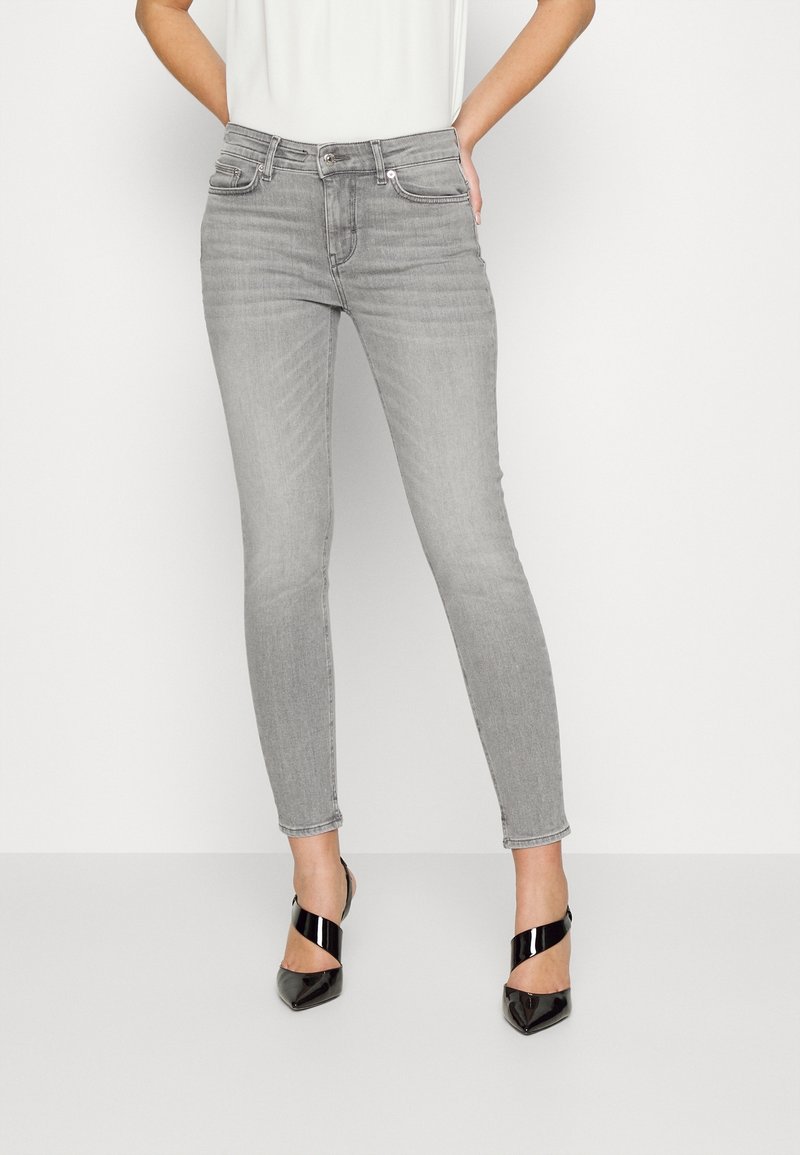 Jeans skinny grises de denim, con un diseño clásico de cinco bolsillos, pasadores para cinturón y cremallera. Combinados con tacones abiertos negros.