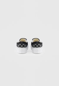 Fekete-fehér sakkmintás, alacsony szárú slip-on sportcipők fehér gumitalppal, hátulról fényképezve, tiszta fehér háttér előtt.