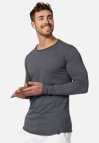 Camisa de manga larga gris de material suave, con un escote redondeado, ajuste slim y un ligero dobladillo curvado. Decorada con una pequeña etiqueta.