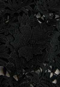 Sort blonde stof med indviklede blomsterdekorationer og teksturerede detaljer, der viser en kombination af tætte og åbne vævemønstre.