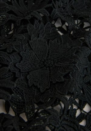 Fekete csipkefehér terítő bonyolult virágmintákkal és texturált részletekkel, szilárd és nyitott szövésű részek kombinációját bemutatva.
