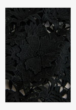 Fekete csipkefehér terítő bonyolult virágmintákkal és texturált részletekkel, szilárd és nyitott szövésű részek kombinációját bemutatva.
