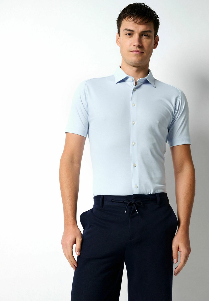 Helles blaues Poloshirt mit kurzen Ärmeln, Kragen und Knopfleiste. Kombiniert mit dunkelblauen Hosen mit elastischem Bund und Kordelzug.