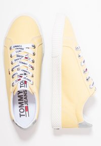 Yellow canvas sneakers with white rubber soles and round laces, featuring "TOMMY JEANS" branding on the laces and insoles.