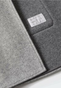 Organisateur en feutre gris avec une texture douce, présentant une étiquette blanche pour les coordonnées et un bord simple cousu.