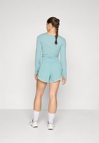Lys blå langermet topp og matchende shorts. Toppen har en tettsittende design, mens shortsen har et elastisk liv og en flytende fasong.