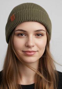 Olive green knitted beanie with ribbed texture and a brown leather tag sewn on the front. Smooth fabric design, fitted style.