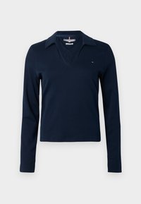 Marineblå langermet polo med V-hals, som har en klassisk krage. Laget av glatt stoff. Lite logo på venstre bryst.