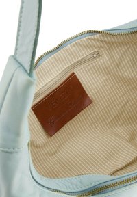 Jasnoniebieska skórzana torebka z wnętrzem wykończonym w paski w odcieniach beżu. Posiada brązową skórzaną metkę z napisem "VENEZIA Genuine Leather" oraz kieszeń na zamek błyskawiczny.