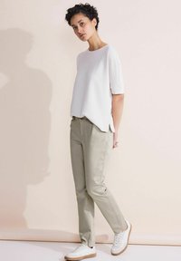 Witte top met korte mouwen en een ontspannen pasvorm, gecombineerd met lichtgroene broek en witte sneakers. Eenvoudig ontwerp zonder zichtbare patronen of accenten.