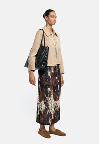 Beżowa zamszowa kurtka z kołnierzem, biała bluzka, długa spódnica w brązowo-czarne wzory oraz brązowe buty wsuwane. Czarna torebka na ramię z guziczkami.