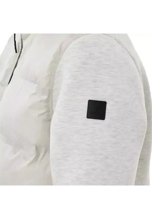 Chaqueta gris claro con un panel frontal acolchado, mangas lisas y un parche de logo negro en el brazo izquierdo para mayor detalle.
