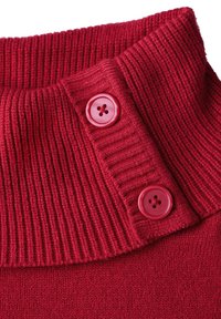 Roter Pullover mit einem gerippten Rollkragen und zwei runden, rosa Knöpfen am Hals. Glatte Textur mit einem Strick-Finish.