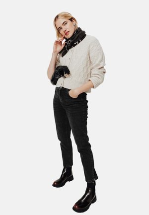 Cardigan crème en maille avec un motif texturé, associé à un jean noir et des bottines en cuir marron. Accessoirisé avec une écharpe noire et une pochette.