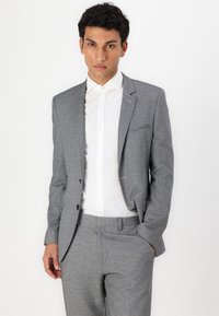Grå tweeddress med et strukturert mønster, som har en en-knapps jakke og slim-fit bukser. Kombinert med en hvit skjorte.