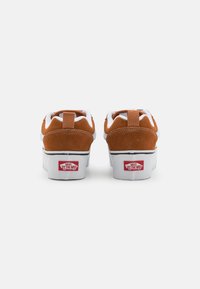 Brune ruskinds sneakers med hvide snørebånd og indvendig foring, med et rødt Vans-logo på hælen og en kraftig hvid sål.