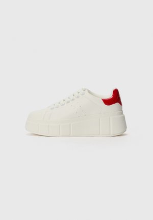 Weiße Sneakers mit einer strukturierten Plateausohle, die einen glatten Körper und einen glänzenden roten Akzent an der Ferse aufweisen. Schnürdesign mit Perforationen.
