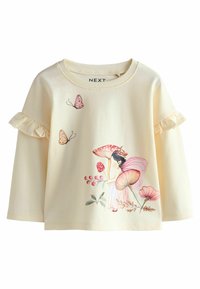 Haut en coton jaune pâle à manches longues, avec des manches volantes. Le design à l'avant comprend une fée entourée de champignons, de fleurs et de papillons.