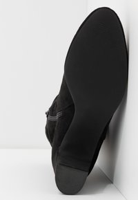 Černé semišové kotníkové boty s hladkou černou gumovou podrážkou, s bočním zipem a texturovaným gripem pro lepší trakci.