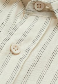 Lichtbeige shirtstof met dunne zwarte strepen, voorzien van een knoopsluiting van lichtgekleurde kunststof, met een gestructureerde weving.